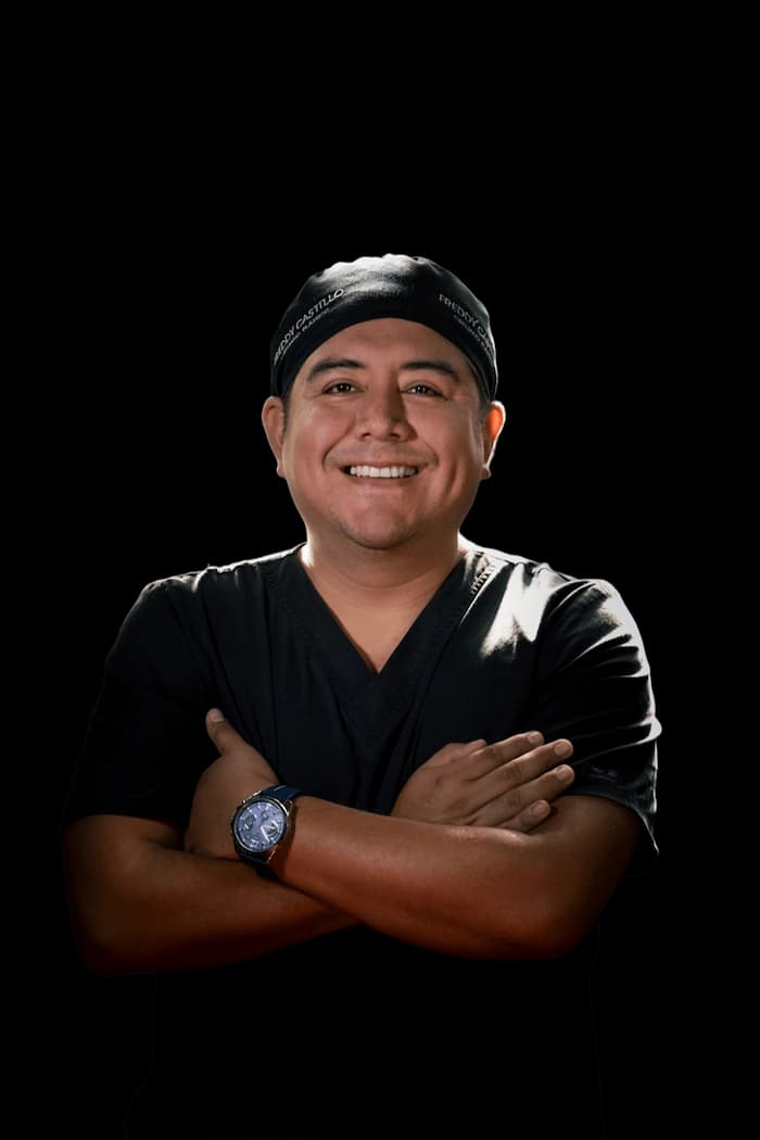 Dr. Freddy Castillo, cirujano plástico en Lima, con uniforme quirúrgico y brazos cruzados